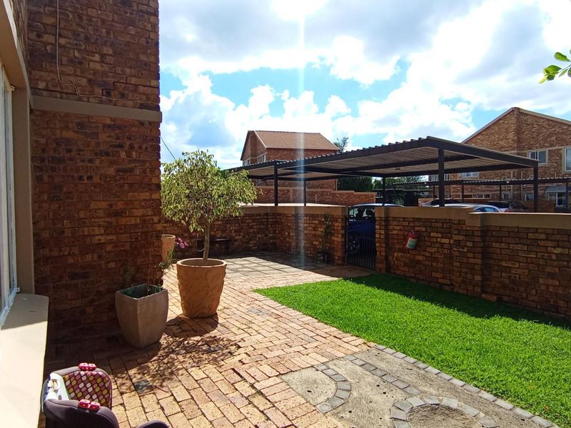 A private rear courtyard featuring a paved patio area, a small lawn, and a covered carport structure enclosed by face brick boundary walls.