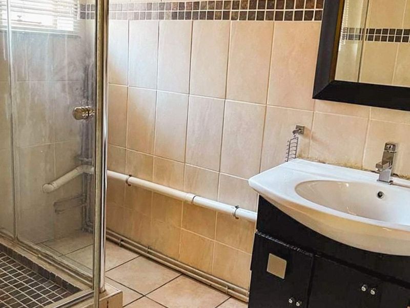 A functional bathroom featuring a shower enclosure, vanity basin, and tiled finishes. The space would benefit from cosmetic updates to modernize the fixtures.