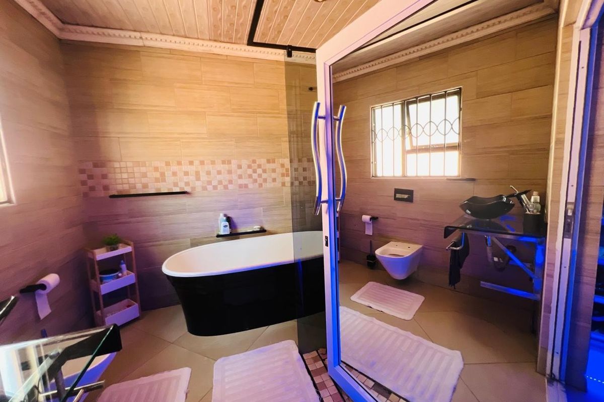 Modern bathroom featuring a freestanding bathtub, wall-mounted toilet, glass vessel sink, and contemporary tiled finishes with a glass shower partition.