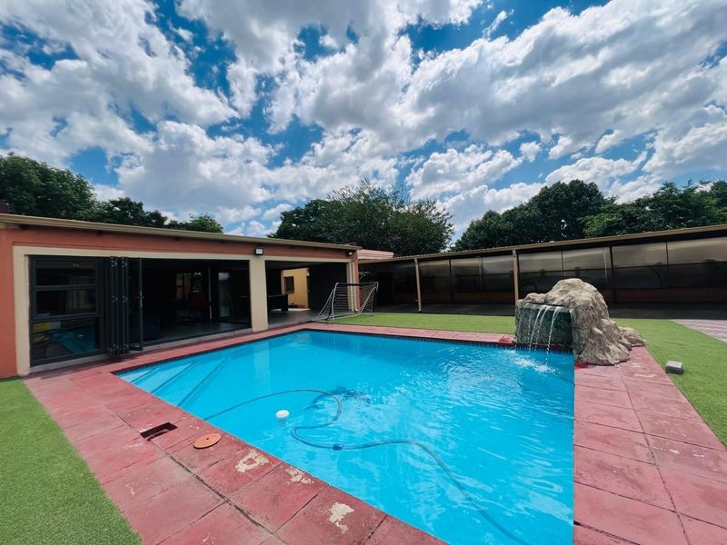 Outdoor pool area featuring a rock water feature, artificial turf, and a covered patio with bi-fold doors for seamless indoor-outdoor living.