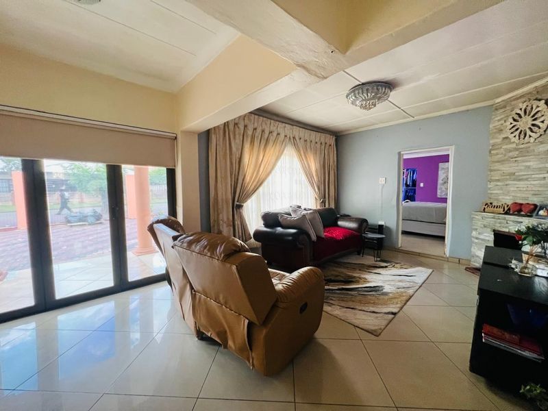 Spacious living room featuring large sliding glass doors, tiled flooring, and a prominent stone-clad fireplace, offering a bright and functional layout.