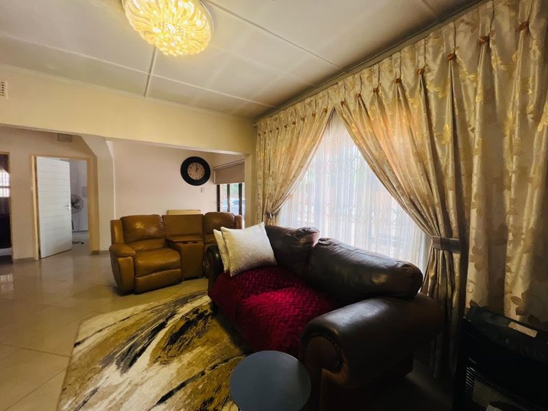 A comfortable living room featuring tiled flooring and large windows with curtains, providing a bright and functional space for relaxation.