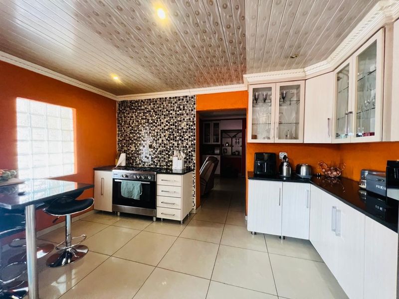 A functional kitchen featuring white cabinetry, dark granite countertops, a mosaic tile backsplash, and a glass block window, providing a bright and practical workspace.