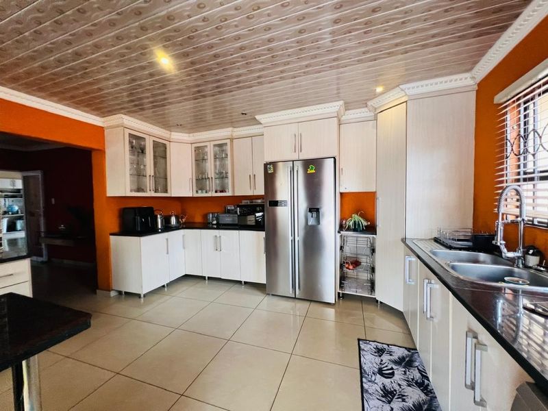 A functional kitchen featuring light-toned cabinetry, dark countertops, a double sink, and tiled flooring with a distinctive patterned ceiling finish.