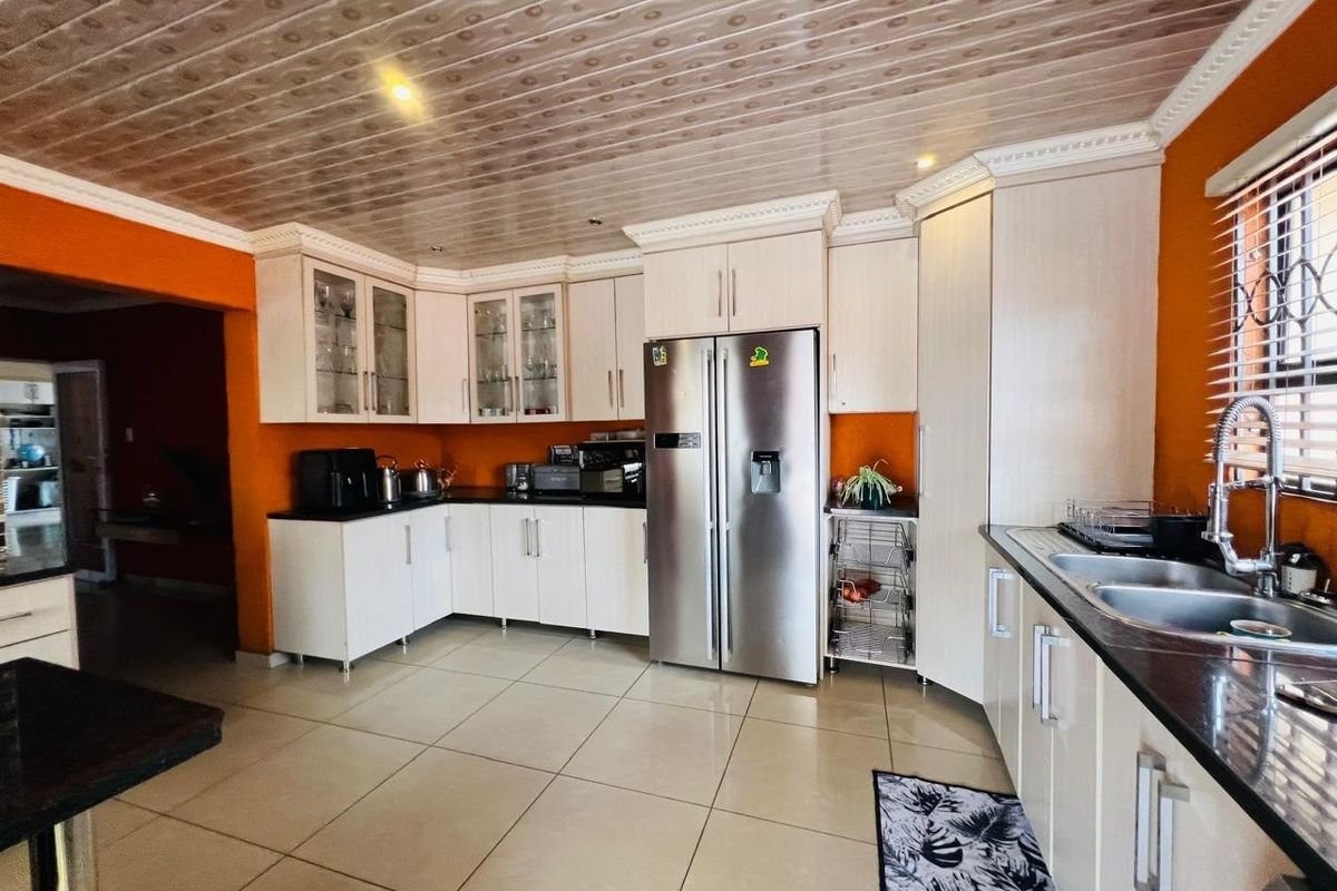 A functional kitchen featuring light-toned cabinetry, dark countertops, a double sink, and tiled flooring with a distinctive patterned ceiling finish.