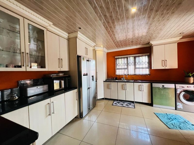 A functional kitchen featuring ample built-in cabinetry, granite countertops, tiled flooring, and a stainless steel sink, with security bars installed on the window.