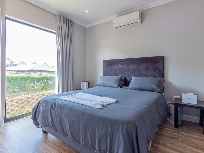 A well-maintained bedroom featuring laminate flooring, an air conditioning unit, and a large sliding glass door providing natural light and garden views.