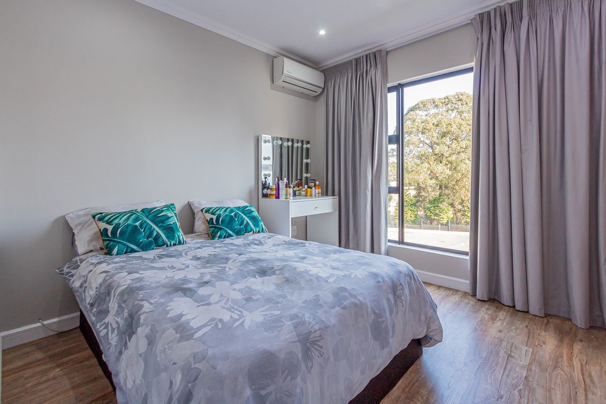 A well-maintained bedroom featuring laminate flooring, a large window with curtains, and a wall-mounted air conditioning unit.