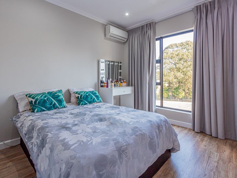 A well-maintained bedroom featuring laminate flooring, a large window with curtains, and a wall-mounted air conditioning unit.