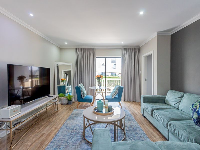 A bright and well-maintained living room featuring laminate flooring, recessed downlighting, and a sliding glass door providing access to the balcony.