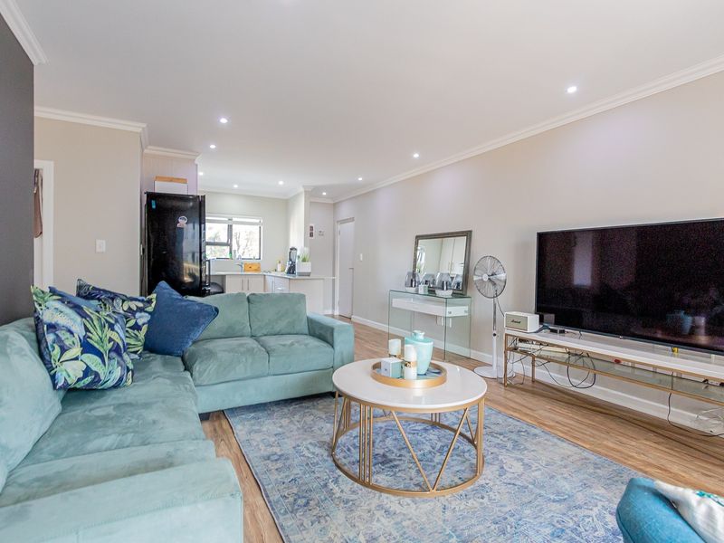 Spacious open-plan living area featuring modern laminate flooring, recessed downlights, and a seamless transition into a functional kitchen space.
