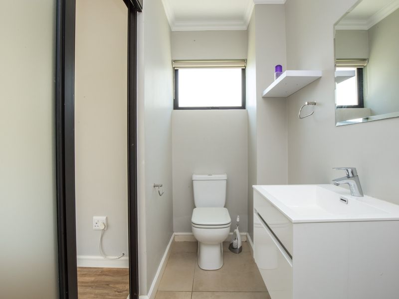 A clean and modern bathroom featuring a white vanity with basin, toilet, and tiled flooring, offering a bright and functional space.