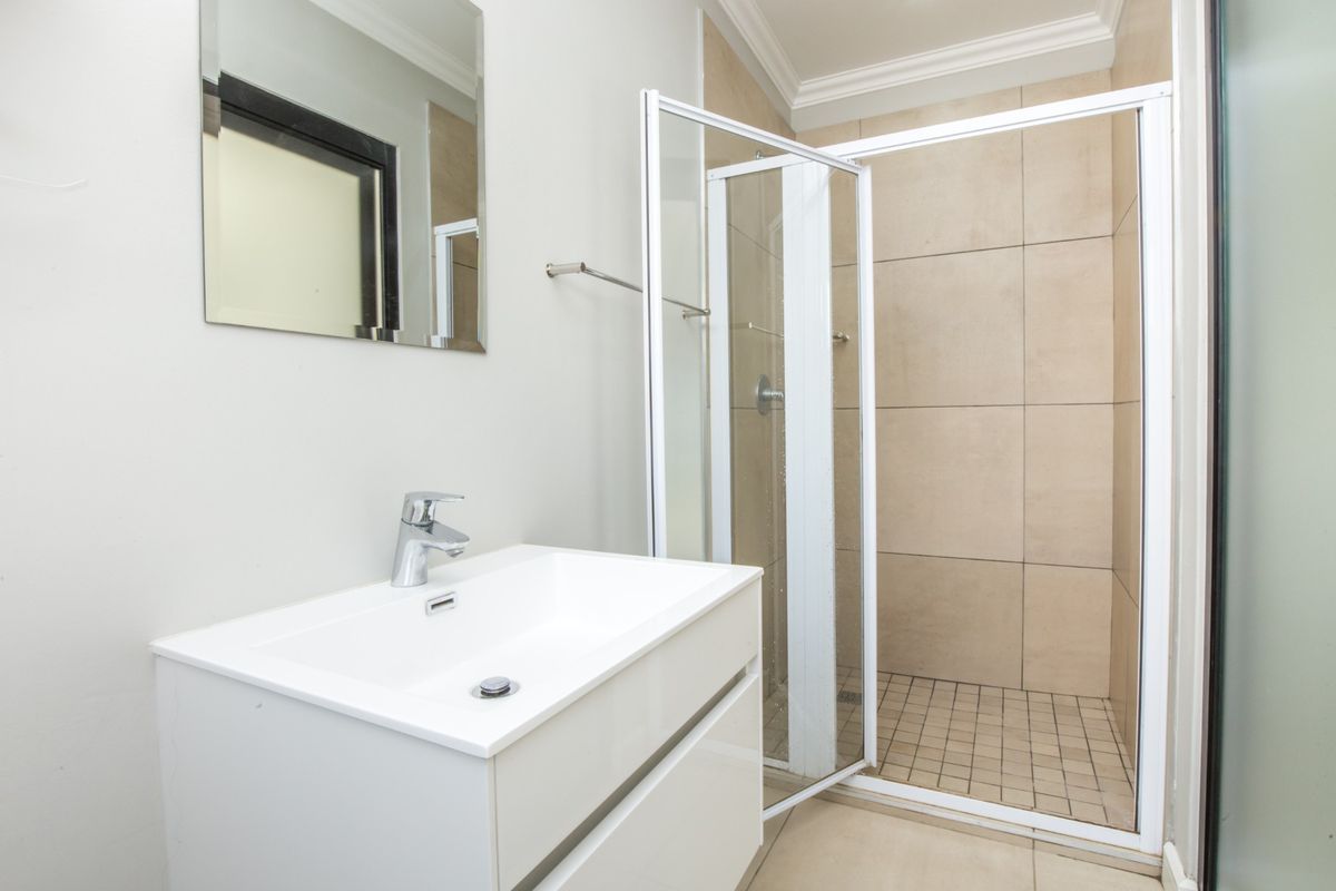 A clean and modern bathroom featuring a white vanity cabinet with a basin, a wall-mounted mirror, and a tiled shower enclosure.