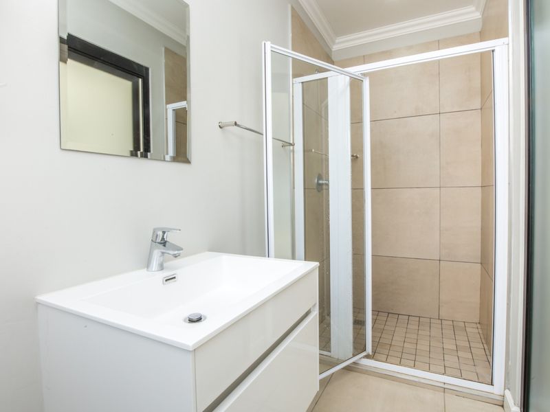 A clean and modern bathroom featuring a white vanity cabinet with a basin, a wall-mounted mirror, and a tiled shower enclosure.