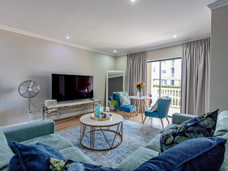 A well-maintained living room featuring laminate flooring, recessed downlighting, and a sliding glass door providing access to an outdoor balcony area.