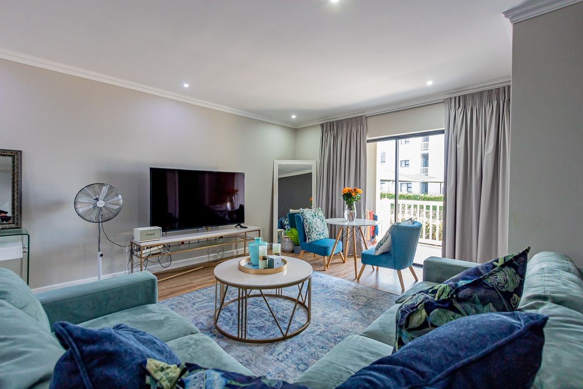 A well-maintained living room featuring laminate flooring, recessed downlighting, and a sliding glass door providing access to an outdoor balcony area.
