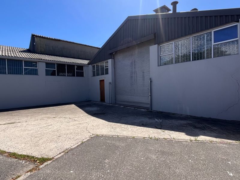 Industrial property exterior featuring a large roller shutter door, concrete driveway, and secure metal roofing, suitable for warehouse or workshop operations.