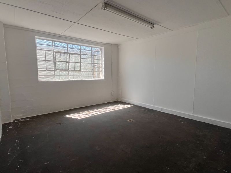 A vacant industrial utility space featuring concrete flooring, a security-barred window, and basic overhead lighting, suitable for storage or workshop use.