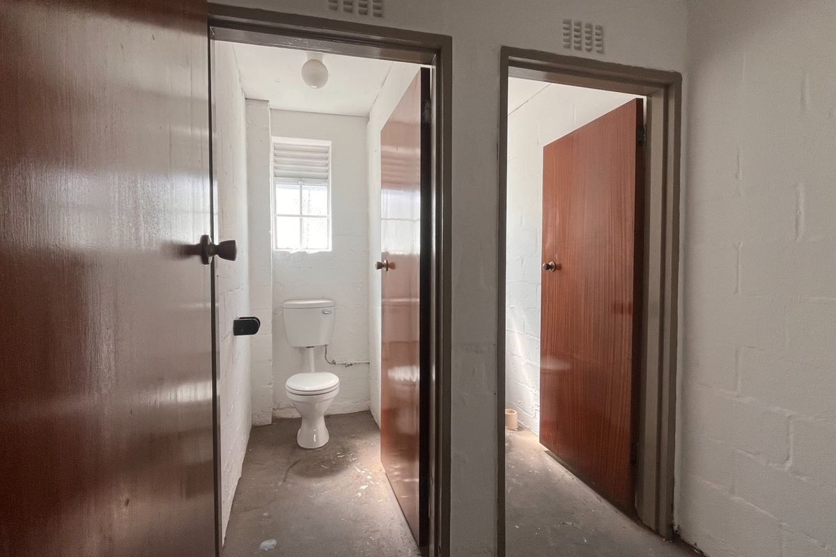 A functional industrial-style bathroom area featuring a toilet, ventilation grilles, and solid core doors, currently in a basic, unfinished condition.