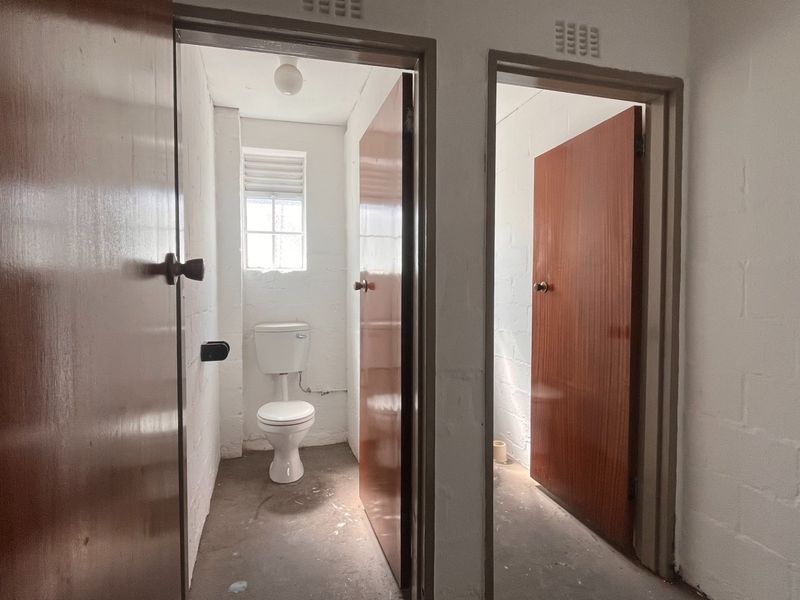 A functional industrial-style bathroom area featuring a toilet, ventilation grilles, and solid core doors, currently in a basic, unfinished condition.