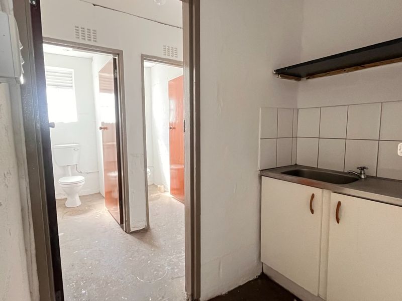 Utility area featuring a stainless steel sink with base cabinetry and tiled splashback, providing access to two separate toilet facilities.