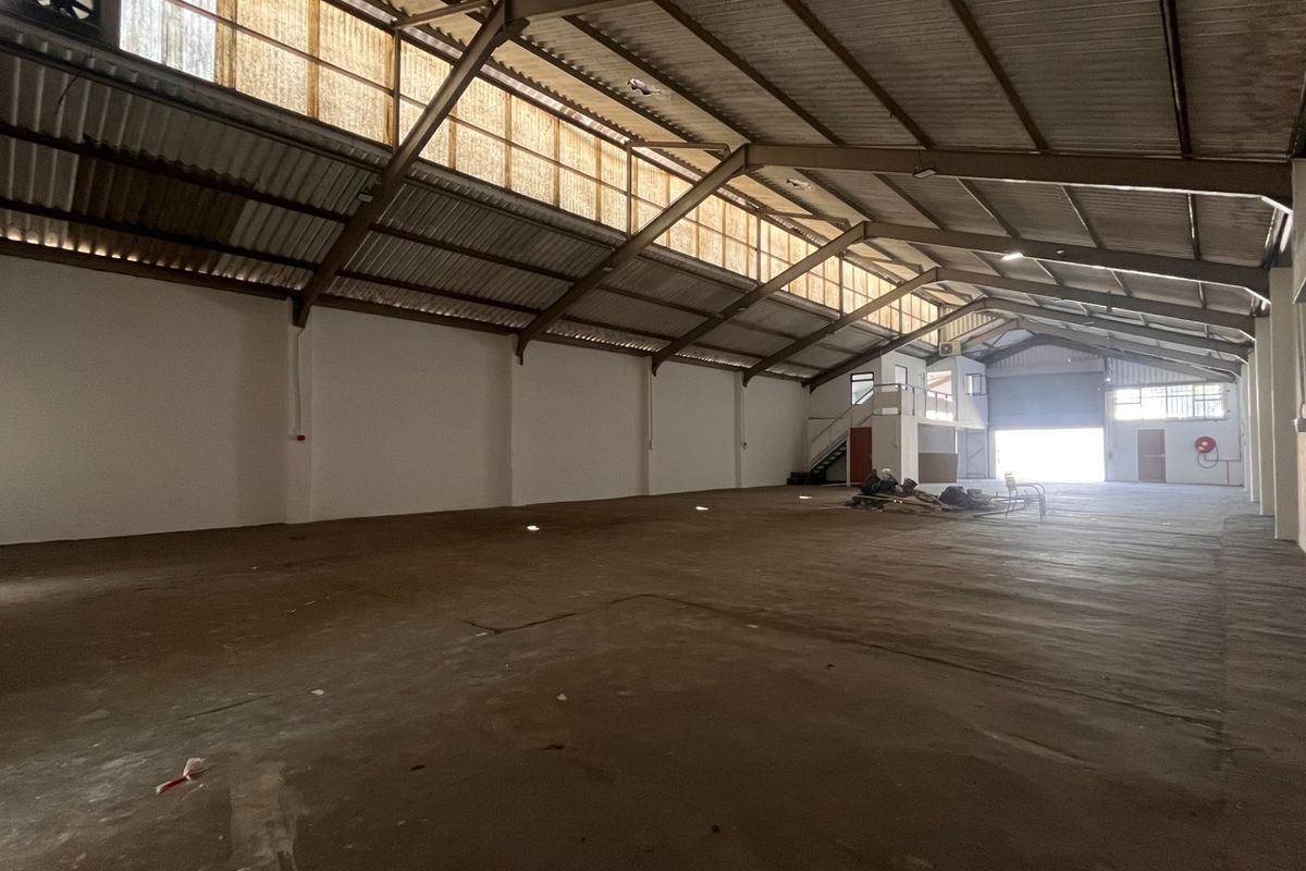 Spacious industrial warehouse featuring high ceilings with exposed steel trusses, clerestory windows for natural light, concrete flooring, and a roller shutter door.