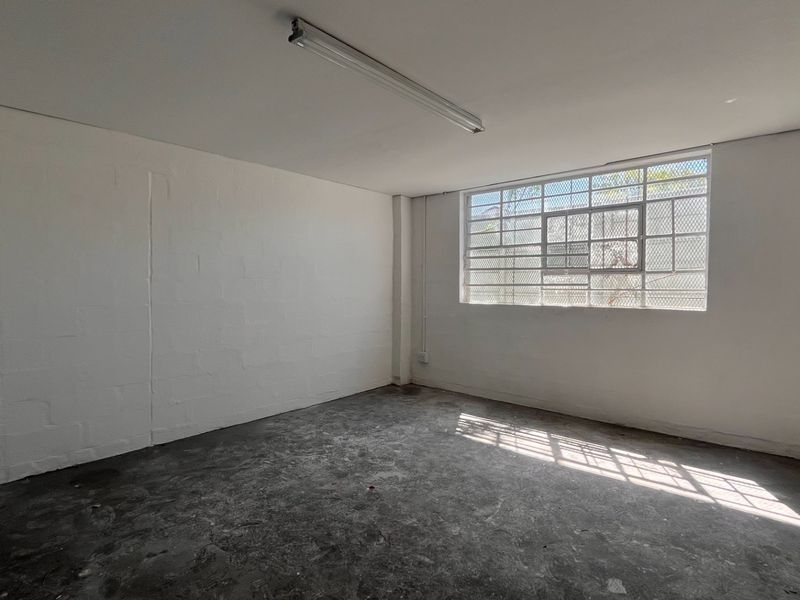 A clean, empty industrial utility space featuring concrete flooring, a security-barred window, and a functional overhead fluorescent light fixture.