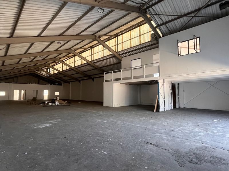 Spacious industrial warehouse featuring high ceilings with exposed steel trusses, a mezzanine level, and durable concrete flooring, suitable for various commercial or storage uses.