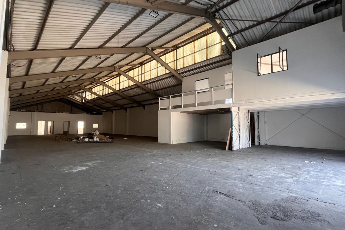 Spacious industrial warehouse featuring high ceilings with exposed steel trusses, a mezzanine level, and durable concrete flooring, suitable for various commercial or storage uses.