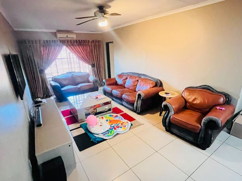 A living room featuring tiled flooring, a ceiling fan, and a wall-mounted air conditioning unit, providing a functional and comfortable space.