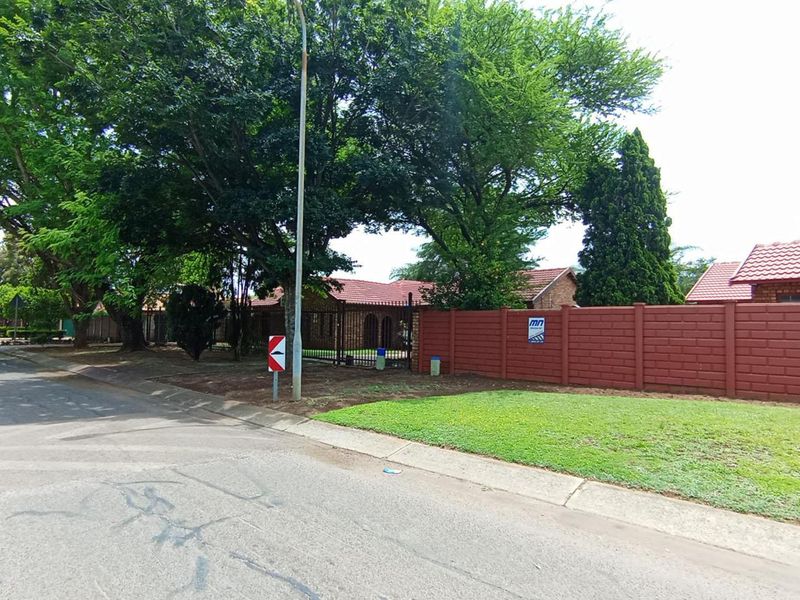 Street view of the property showing the front boundary wall, mature trees, and access gate to the residential premises.