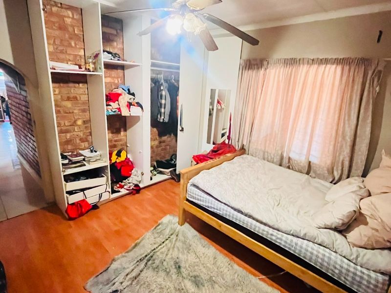 A bedroom featuring built-in cupboards with exposed brick detailing, a ceiling fan, and laminate flooring.