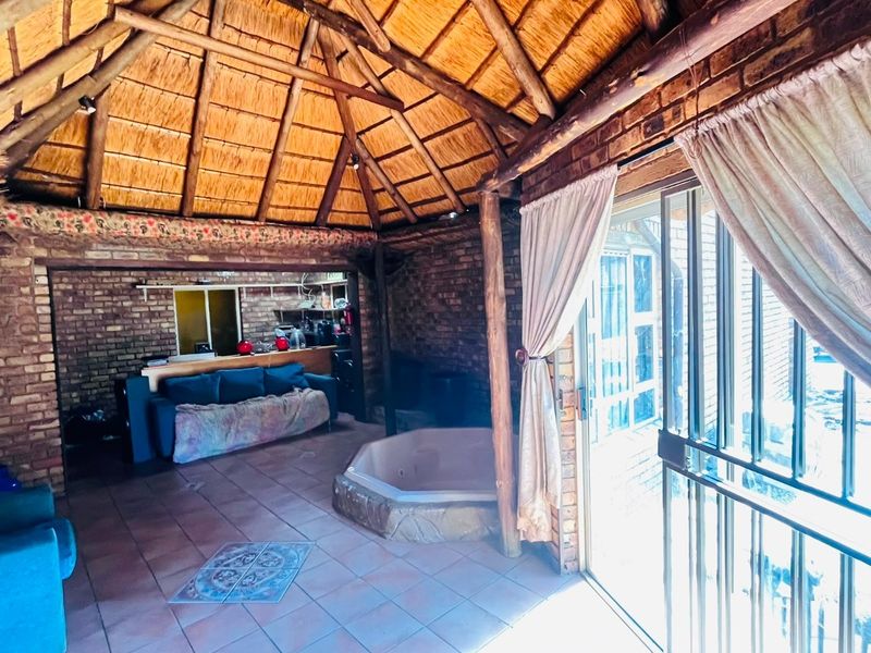 Open-plan living area featuring a unique thatched roof with exposed rafters, brick walls, tiled floors, and a built-in spa bath.