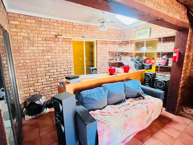 A rustic living room featuring exposed brick walls, timber ceiling beams, and terracotta floor tiles, offering a warm and character-filled living space.