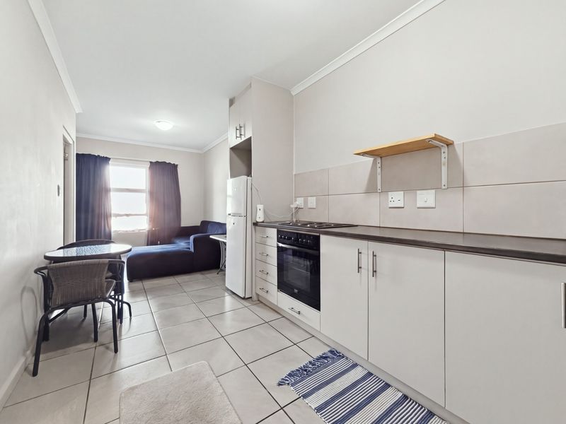 Open-plan living area featuring a functional kitchen with built-in cabinetry, oven, hob, and tiled flooring, seamlessly connecting to the living space.