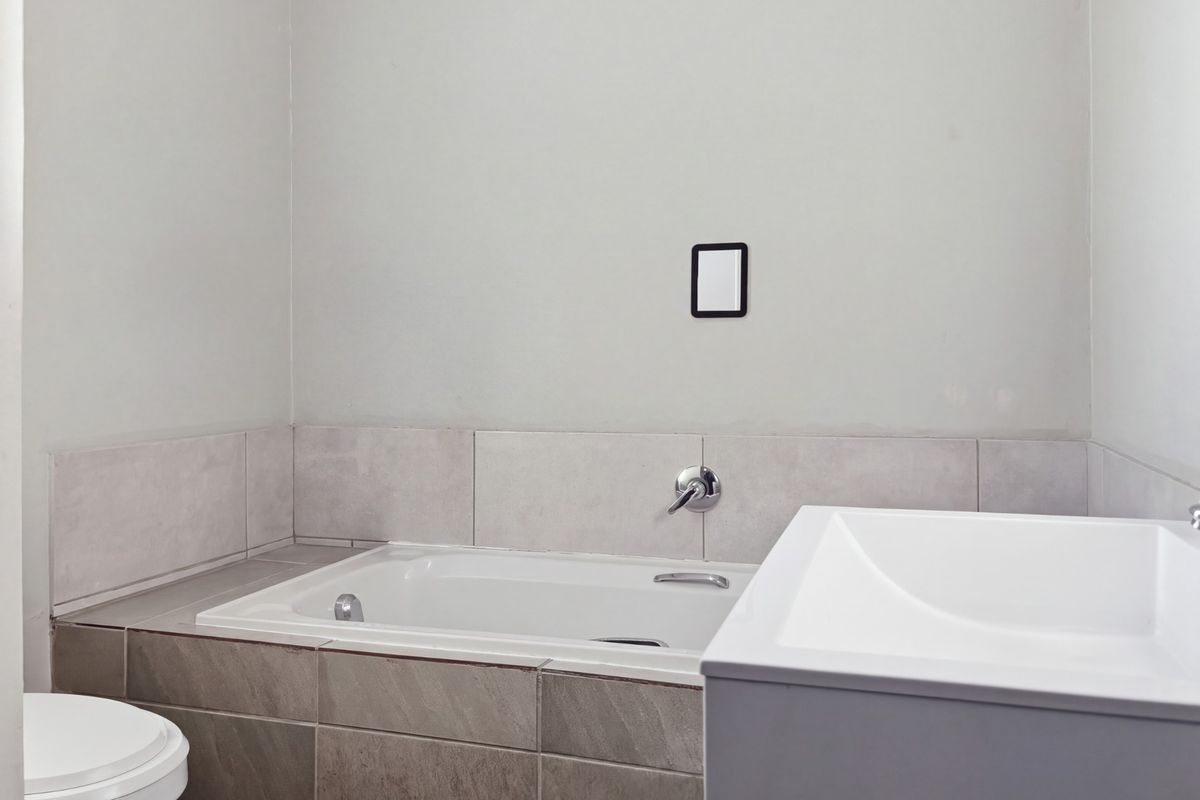 A clean, modern bathroom featuring a built-in bathtub with wall-mounted mixer, a vanity basin, and a toilet with neutral tiled finishes.