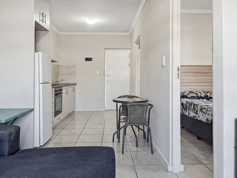 Open plan kitchen and living area featuring tiled flooring, built-in cabinetry, and an integrated oven, with direct access to an adjacent bedroom.