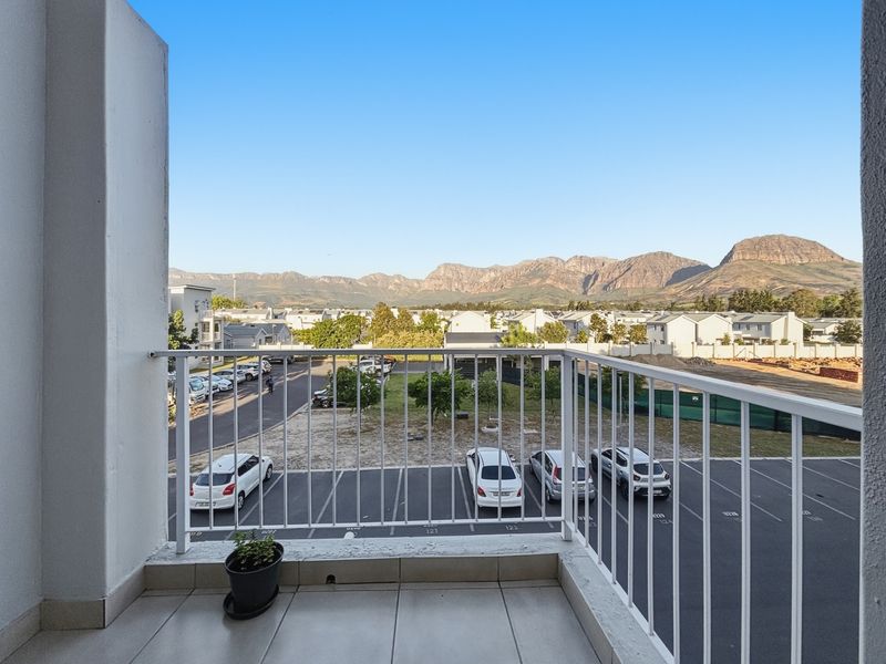 A private balcony featuring tiled flooring and a metal balustrade, offering expansive views of the surrounding neighbourhood and mountain range.