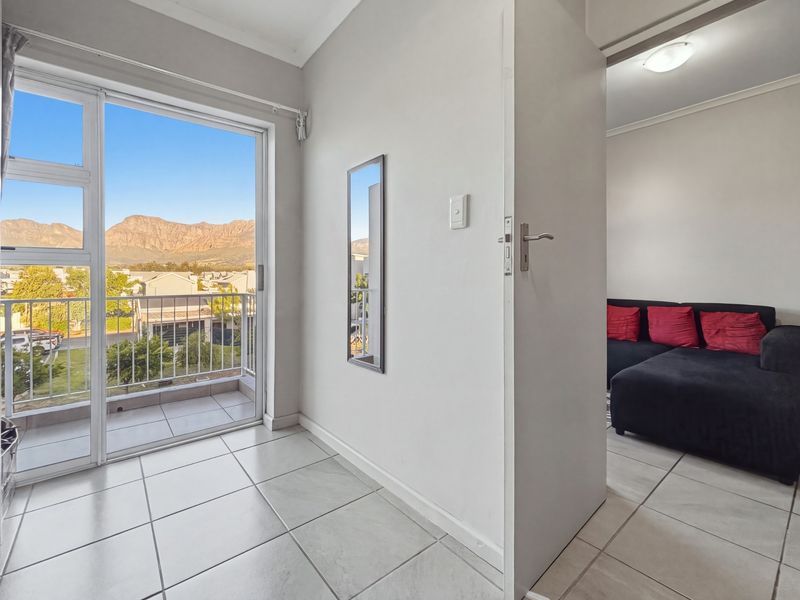 A bright living area featuring tiled floors and a sliding glass door that opens onto a balcony with scenic mountain views.