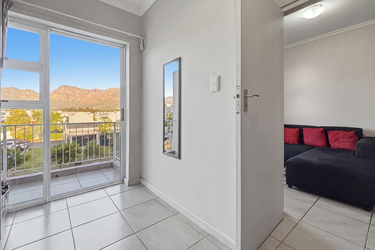 A bright living area featuring tiled floors and a sliding glass door that opens onto a balcony with scenic mountain views.