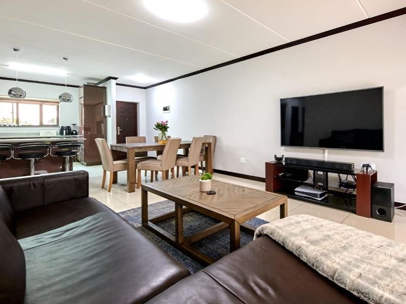 Spacious open-plan living area featuring a modern kitchen with a breakfast bar, dining space, and comfortable lounge area with tiled flooring throughout.