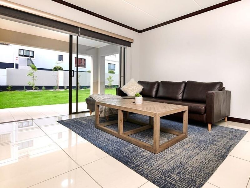 Bright living room featuring large sliding glass doors that open onto a private patio and garden area, with modern tiled flooring throughout.