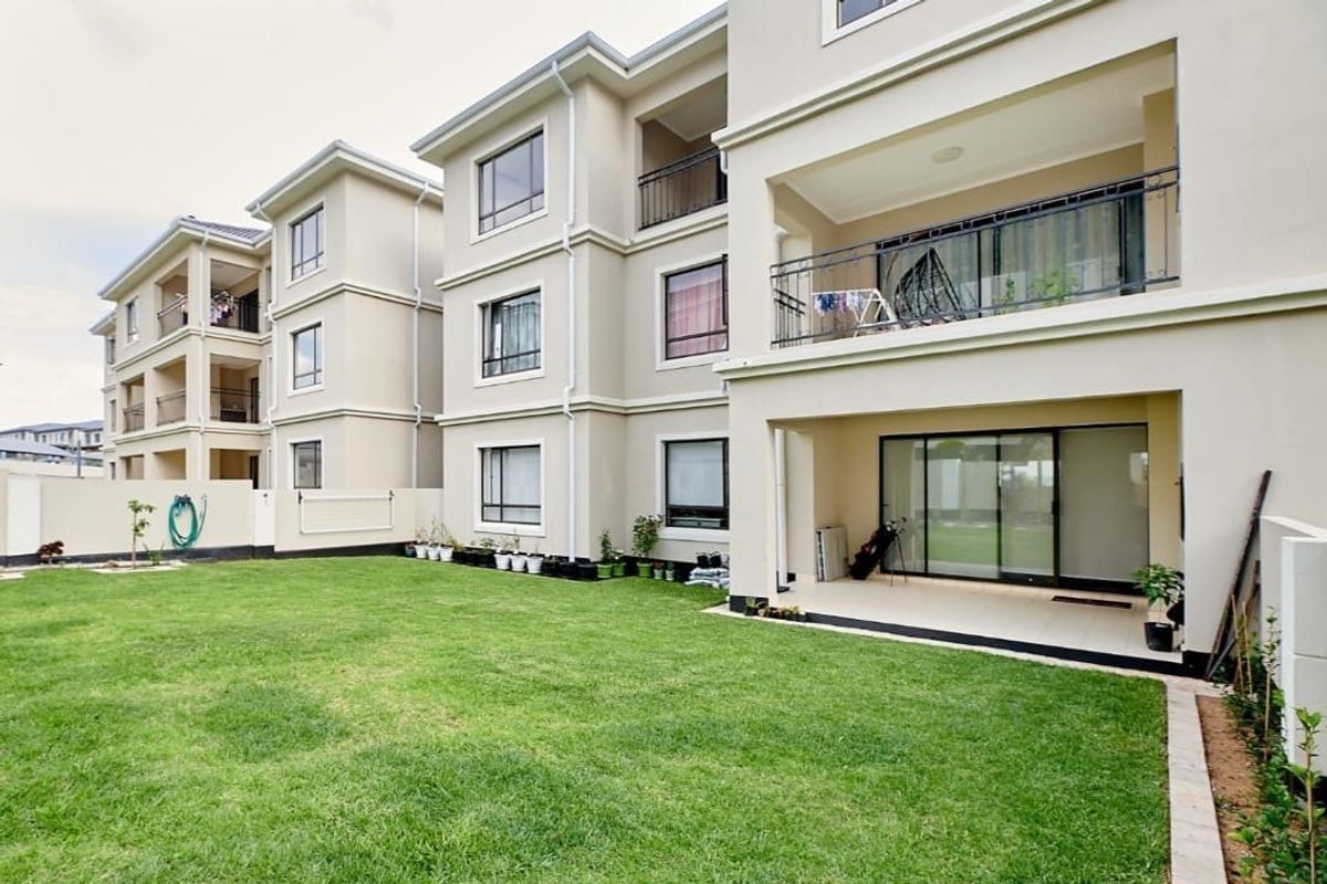 Rear view of a modern apartment complex featuring private ground floor patios, upper-level balconies with wrought iron railings, and a well-maintained communal lawn area.