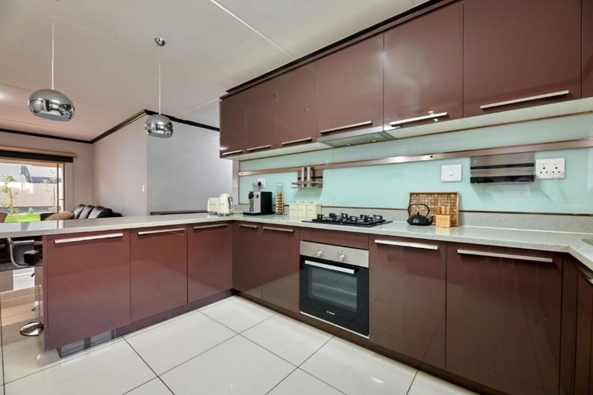 Modern kitchen featuring high-gloss brown cabinetry, stone countertops, a glass splashback, and integrated stainless steel appliances, including a gas hob and oven.