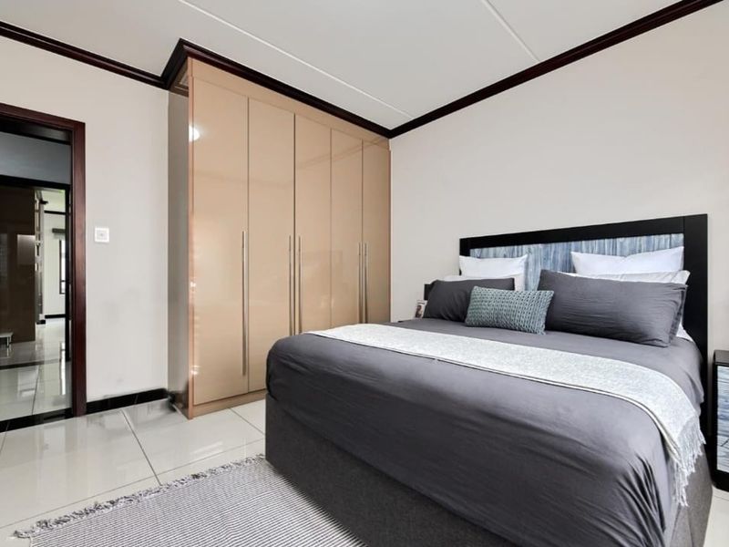 A well-maintained bedroom featuring glossy built-in cupboards, neutral tiled flooring, and dark crown molding accents.