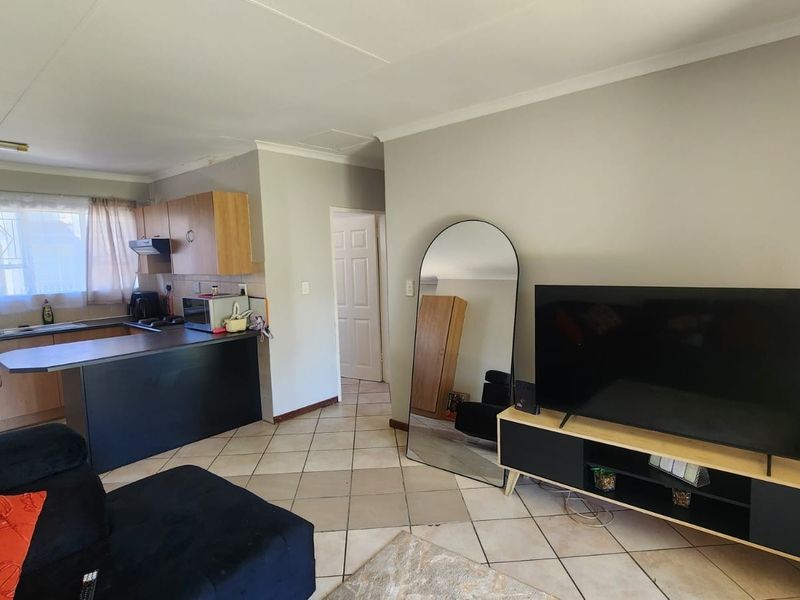 Open-plan living area featuring a functional kitchen with built-in cabinetry and tiled flooring throughout, offering a versatile space for living and dining.