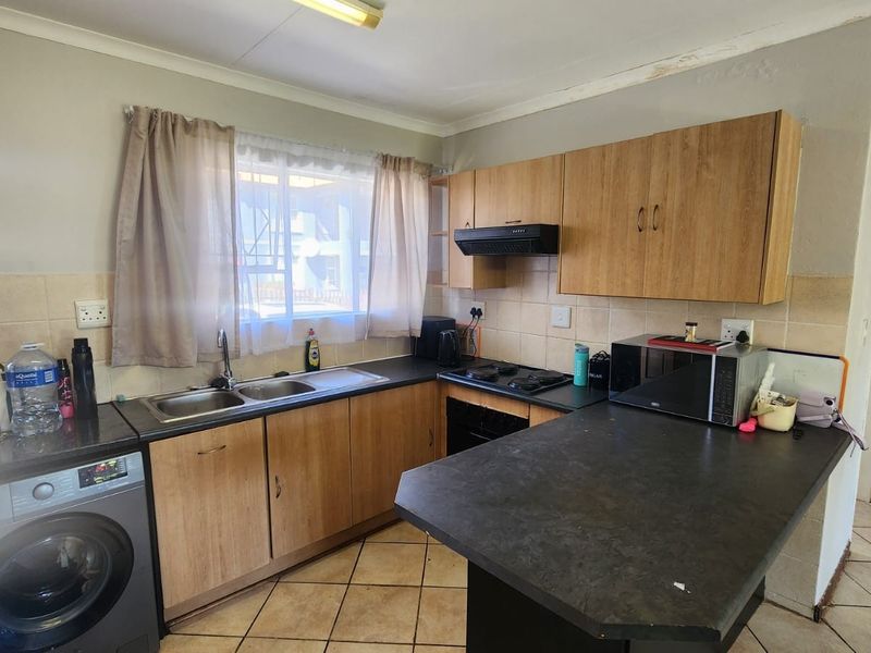 A functional kitchen featuring laminate cabinetry, dark countertops, a double sink, and built-in cooking appliances, with tiled flooring and backsplash.