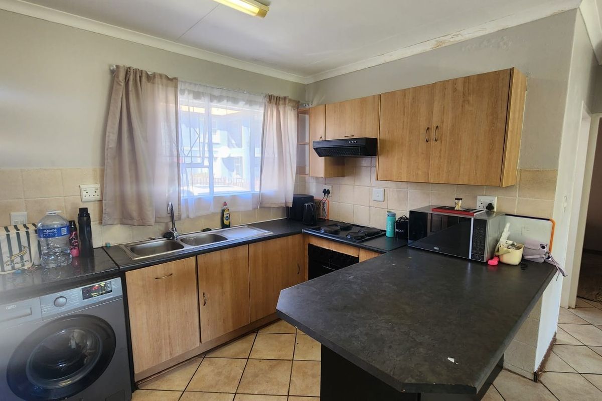 A functional kitchen featuring laminate cabinetry, dark countertops, a double sink, and built-in cooking appliances, with tiled flooring and backsplash.