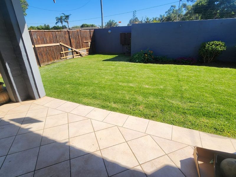 A private outdoor patio area featuring tiled flooring, a well-maintained lawn, and a combination of boundary wall and wooden fencing.