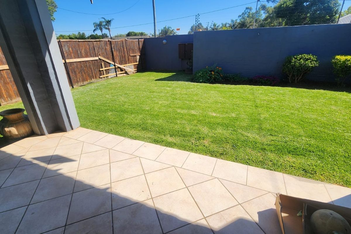 A private outdoor patio area featuring tiled flooring, a well-maintained lawn, and a combination of boundary wall and wooden fencing.